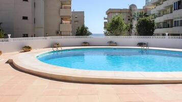 Une piscine dotée d’une terrasse carrelée, entourée d’une clôture blanche et agrémentée de plantes en pot.