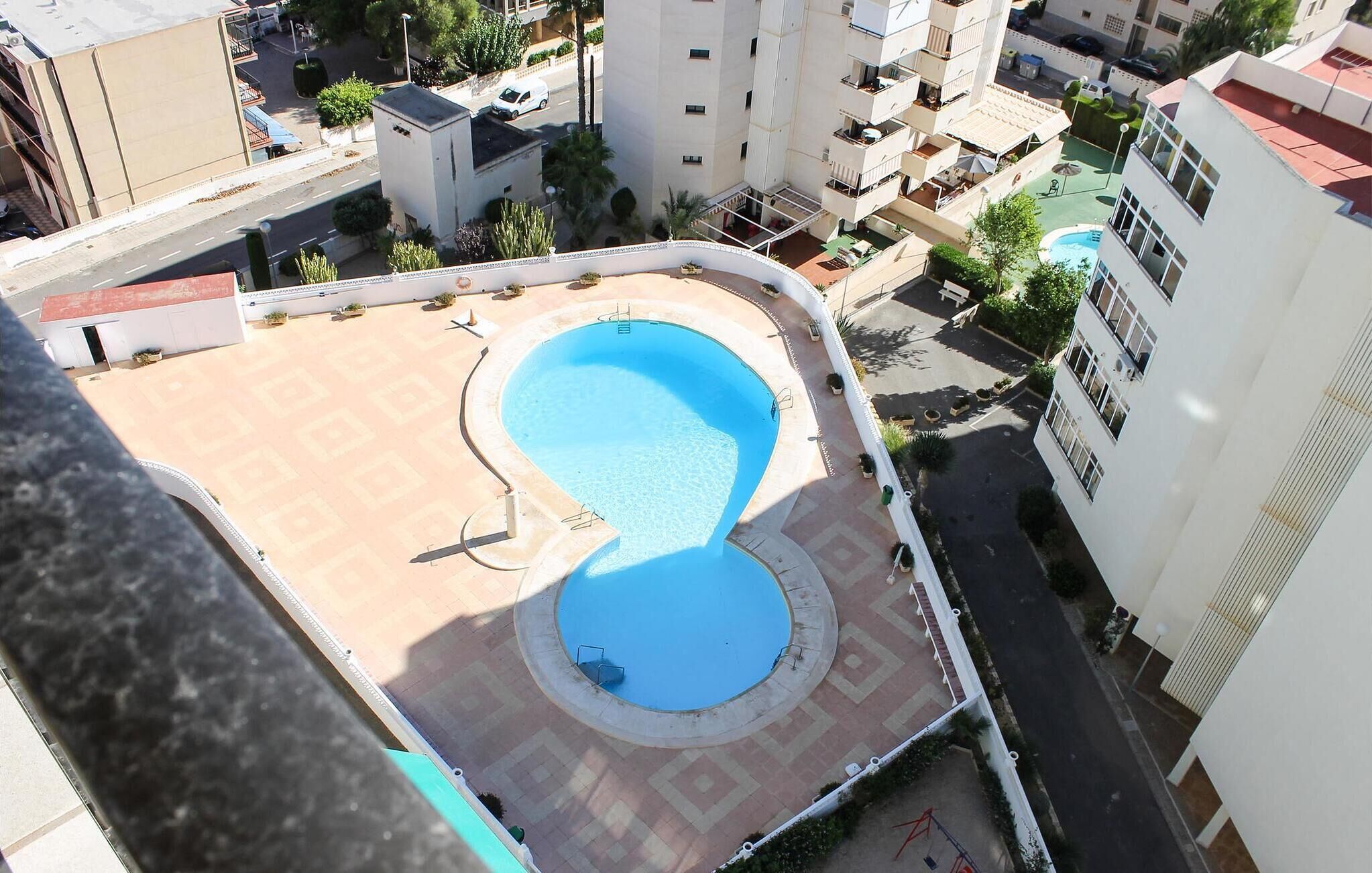 A rooftop pool with a curved design, surrounded by a low wall and a paved area.
