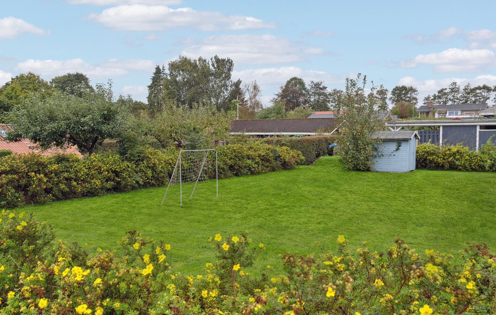 A well-maintained lawn with a soccer goal, surrounded by dense shrubbery and trees.