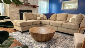 Una sala de estar con un sofá seccional color crema, una mesa de centro de madera y un tapete estampado.