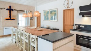 A modern kitchen with a wooden island, white cabinetry, and a black countertop. There are pendant lights, a clock, and a toaster on the counter. - Lovely home in Saint-Vaast-la-Hougue with WiFi (Saint-Vaast-la-Hougue)
