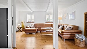 Een ruime woonkamer met een grote, L-vormige bruine leren bank, een houten salontafel en een geweven mand.