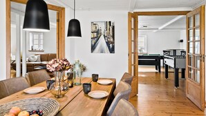 Een eethoek met een houten tafel gedekt voor vier personen, een vaas met bloemen en een schilderij aan de muur.