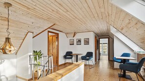 Een moderne loft met houten vloeren, een houten plafond en een trap naar een entresol. Er zijn twee blauwe stoelen, een kleine tafel en een hangende lamp.