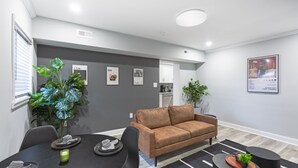Una sala de estar moderna con un sofá marrón, una mesa de comedor preparada para cuatro personas y una cocina al fondo.