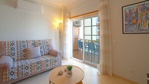 A living room with a patterned sofa, a round coffee table with a plant, and a large window with a view of the outside. - Sunny Beach Treasure by Interhome (Armação de Pêra)