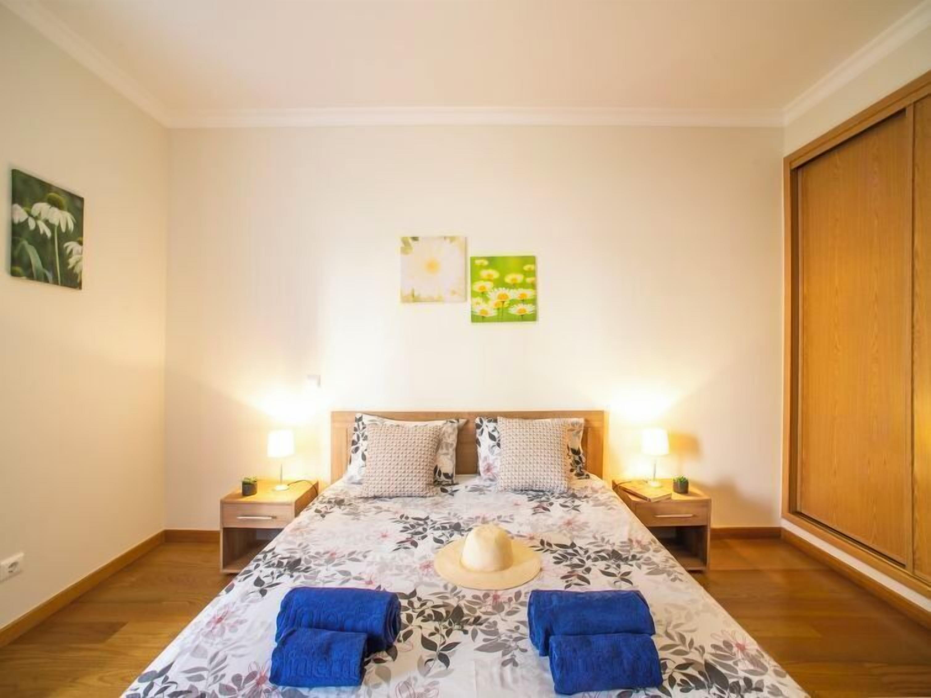 A hotel room with a bed, two nightstands, a wooden wardrobe, and floral wall art.
