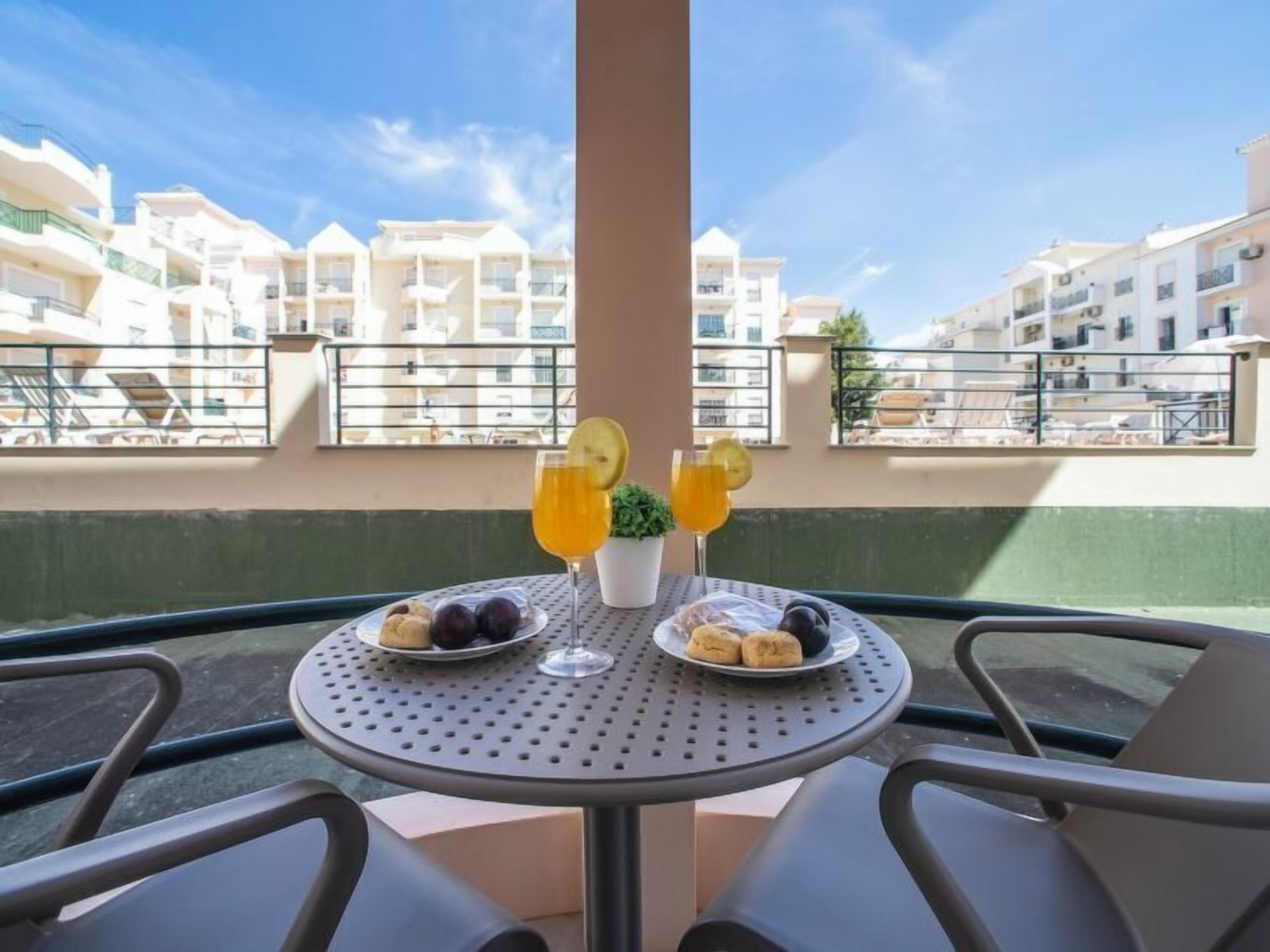 Une table dressée avec un repas et des boissons sur un balcon donnant sur un quartier résidentiel.