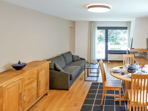 A modern living room with a sofa, wooden cabinet, and a dining area with a table set for two. - Résidence La Fenière 03 by Interhome (Crans-Montana)