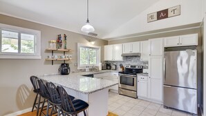 Una cocina moderna con armarios blancos, un refrigerador de acero inoxidable, un horno empotrado y una isla de granito con taburetes de bar.