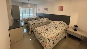 A hotel room with two beds, a desk, a chair, a TV, and a window with a view of the outside.