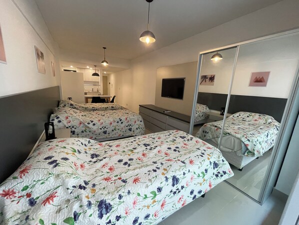 A hotel room with two beds, a desk, a chair, a mirror, and a television.