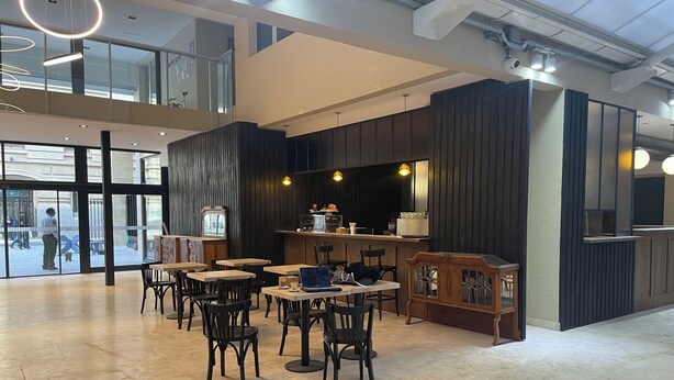 A spacious indoor area with multiple tables and chairs, a counter with a display, and a large window overlooking the street.