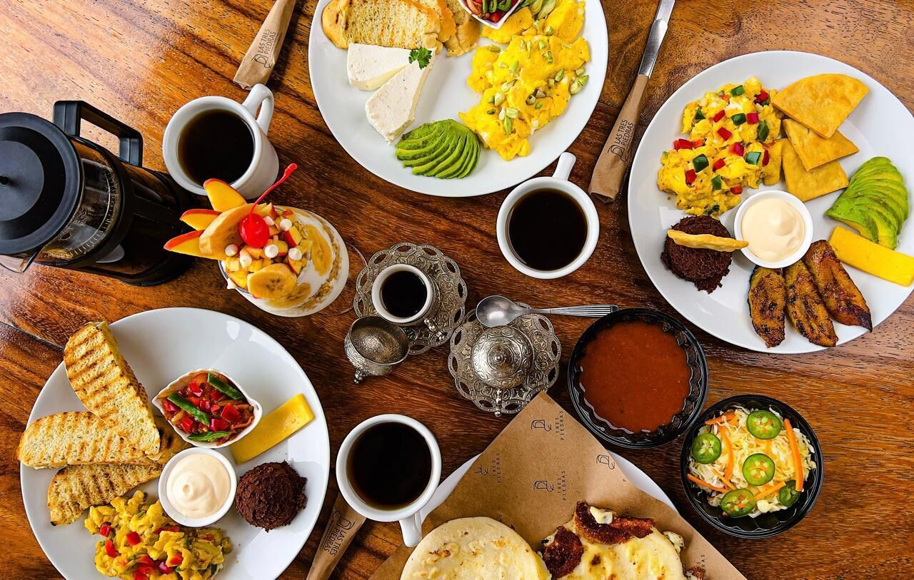 A breakfast spread with various dishes, drinks, and a coffee maker on a wooden table.