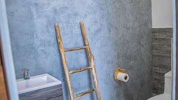 Un bany amb una escala de fusta adossada a una paret amb relleu, un lavabo i un vàter.