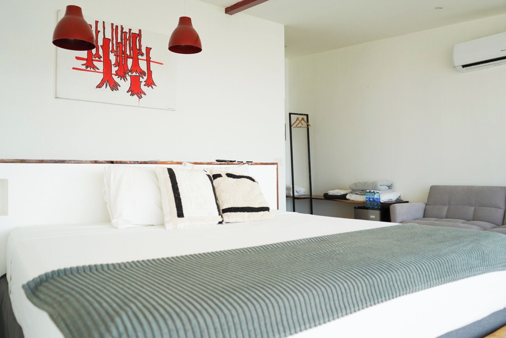 Ein Hotelzimmer mit einem großen Bett, einem Schreibtisch mit Stuhl, einem Wasserspender und einer Wand-Klimaanlage.