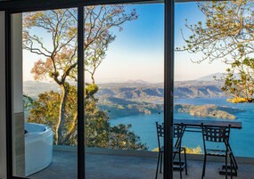 Un balcón con mesa y sillas que ofrece una vista panorámica de un lago y montañas.
