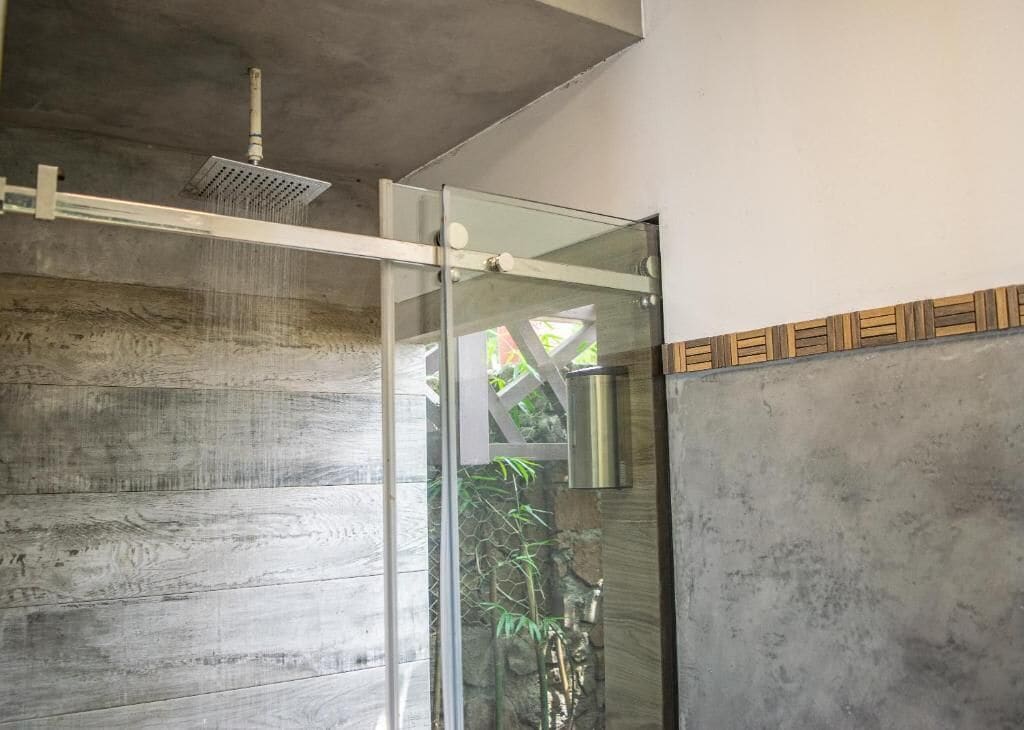 A modern bathroom with a glass shower enclosure, a wooden floor, and a stone wall.