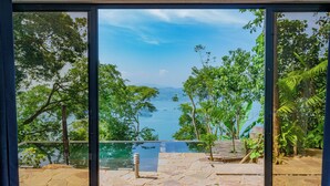 A view from a room with a large window overlooking a pool and lush greenery.
