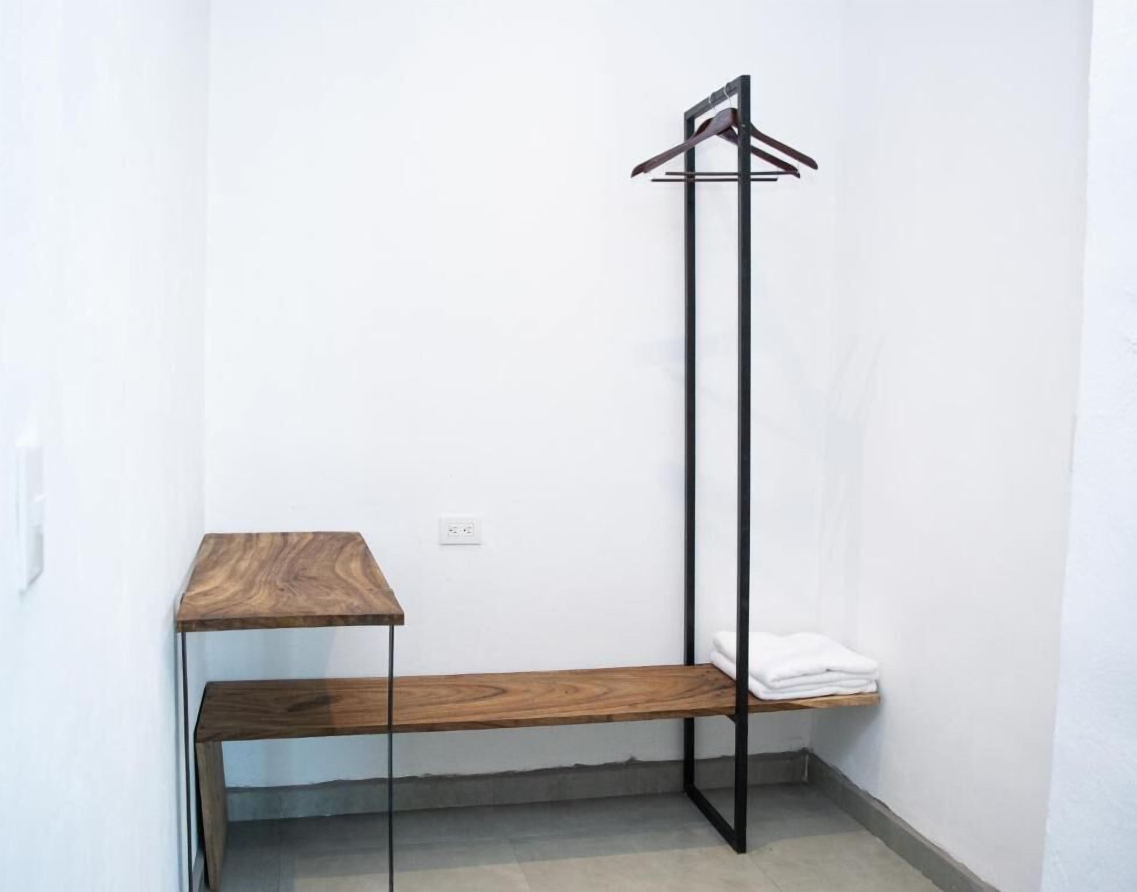 Habitación de esquina con un banco de madera, un perchero y una pequeña mesa.