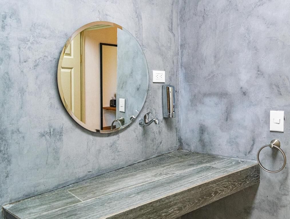 Une salle de bain avec un miroir rond, un meuble-lavabo en bois et un porte-serviettes.