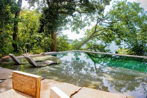 A tranquil outdoor pool area surrounded by lush greenery, with stone benches and a clear view of the sky.