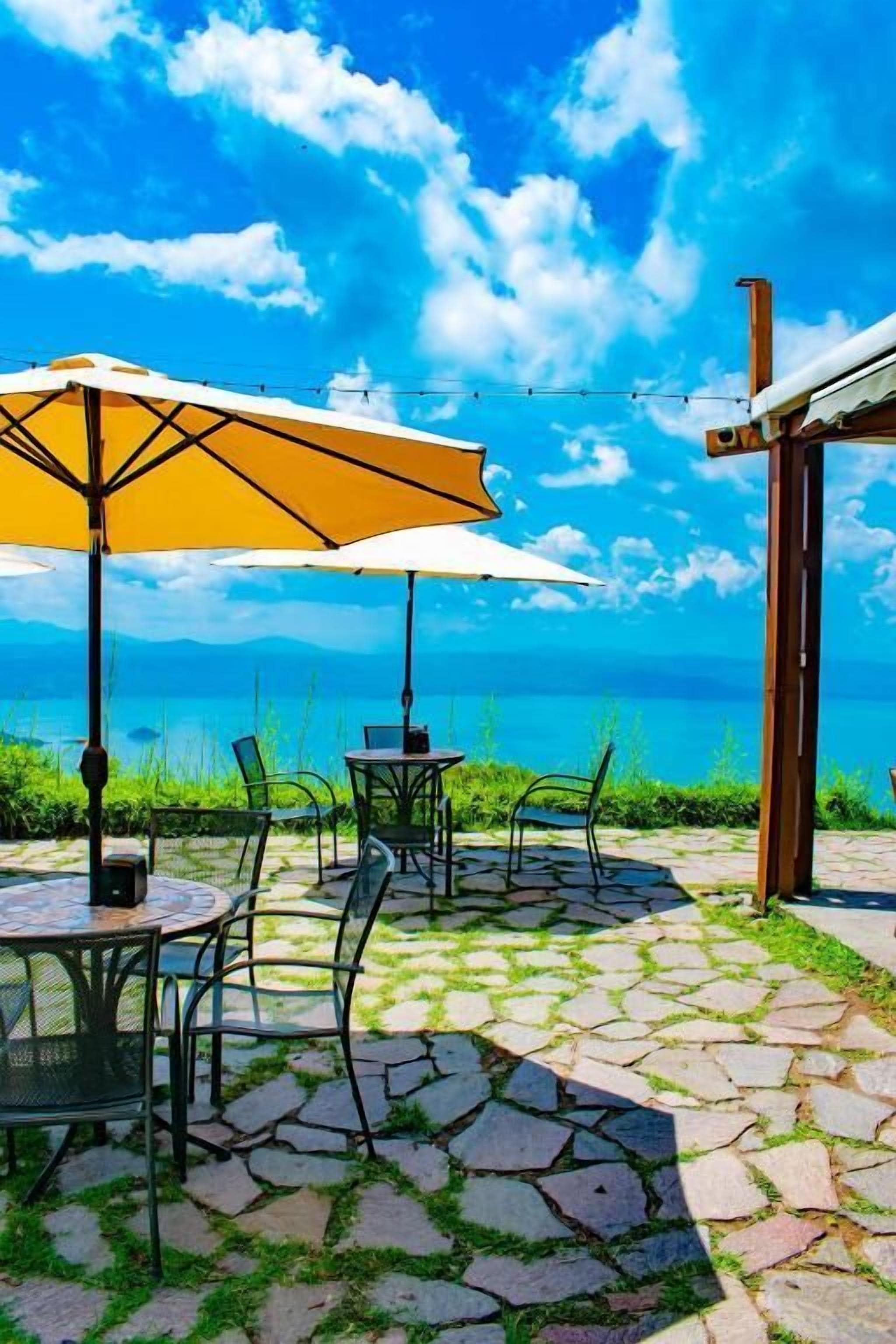 Un patio al aire libre con suelo de piedra, sillas de metal y un paraguas amarillo.