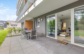 Eine moderne Wohnung mit einer Terrasse, ausgestattet mit Tisch und Stühlen, einer Glasschiebetür zum Wohnzimmer und Blick auf die umliegende Nachbarschaft.