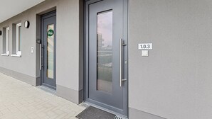 Eine moderne Gebäudefassade mit grauem Außenbereich, einer Tür mit Griff und einem Fenster mit Blick auf Gebäude.