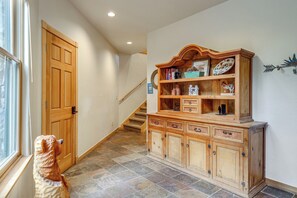 Een hal met een houten trap, een groot houten kast met lades, en een decoratief wandobject.