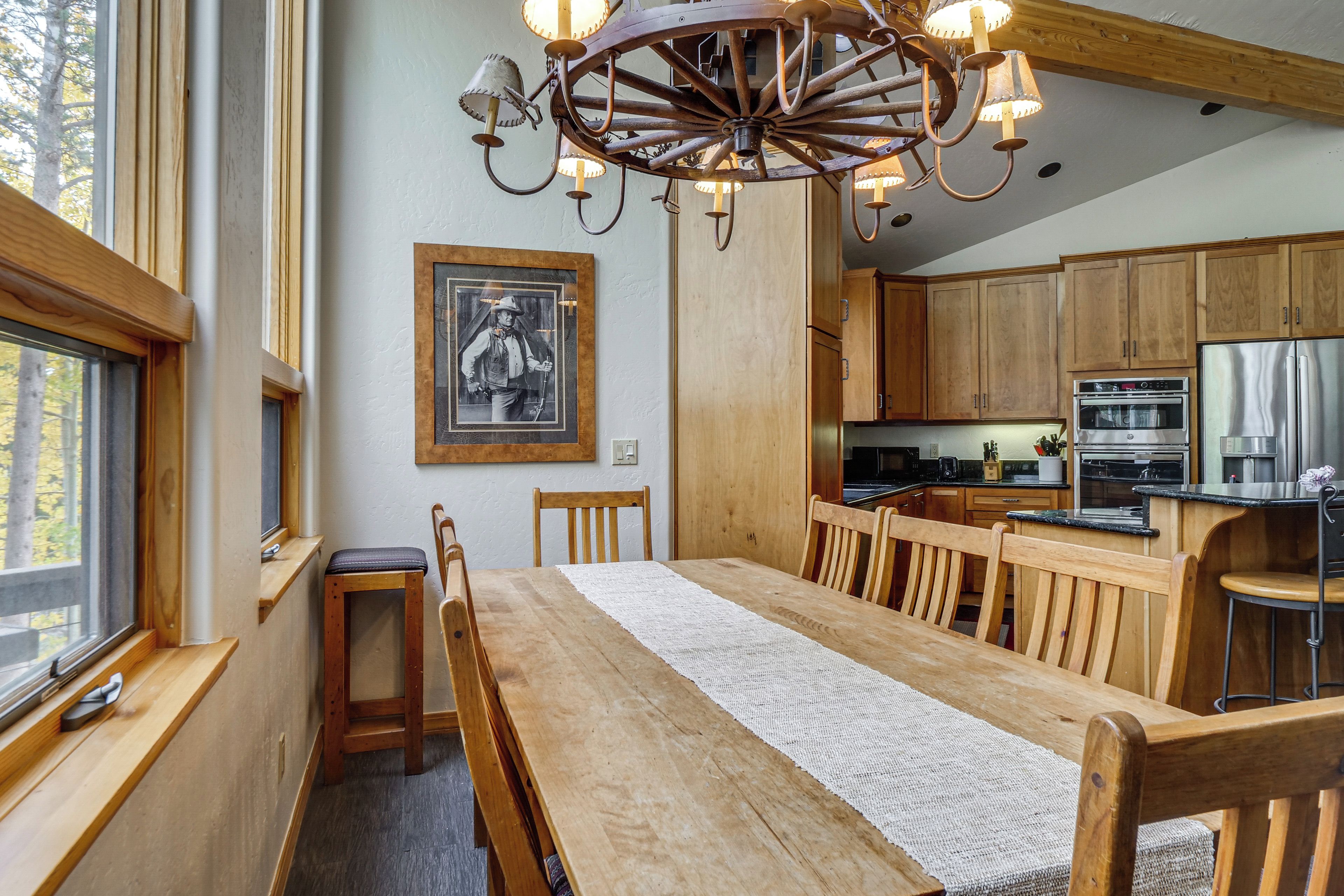 Een houten eettafel met stoelen, een kroonluchter en een keuken met houten kastjes.