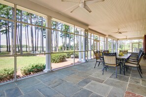 Eine überdachte Terrasse mit Steinböden, großen Fenstern und Sitzgelegenheiten im Freien.