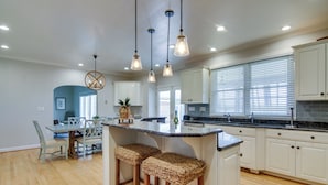 Una cocina moderna con armarios blancos, encimera de granito y una isla central con taburetes de bar.