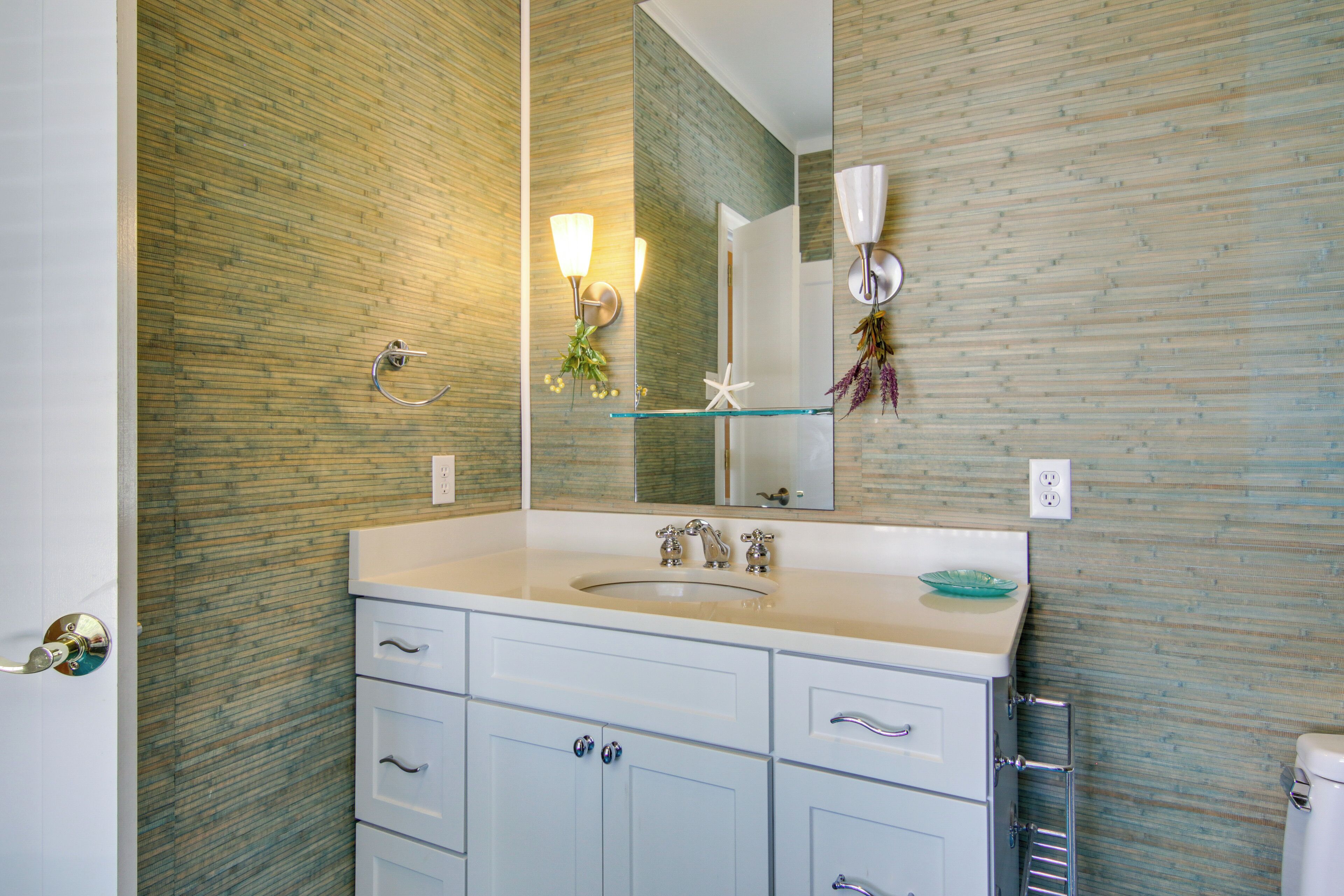 A bathroom with a glass shelf, white cabinets, and a mirror.