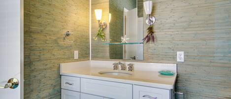 A bathroom with a glass shelf, white cabinets, and a mirror.