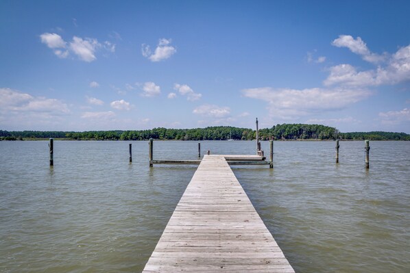 Eine Holzstege, der sich in ruhiges Wasser erstreckt, mit blauem Himmel darüber.
