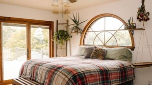Un dormitorio con una cama grande, una banca, una ventana con vistas y una planta en un estante.