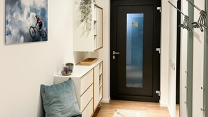 A modern hallway with a dark door, a bench with a cushion, a small plant, and a framed picture on the wall.