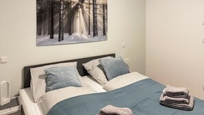 A hotel room with a bed, pillows, a blanket, and a folded towel on the bed.