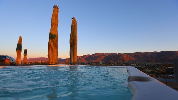 Una piscina amb vista a cactus alts i esvelts i muntanyes al fons.
