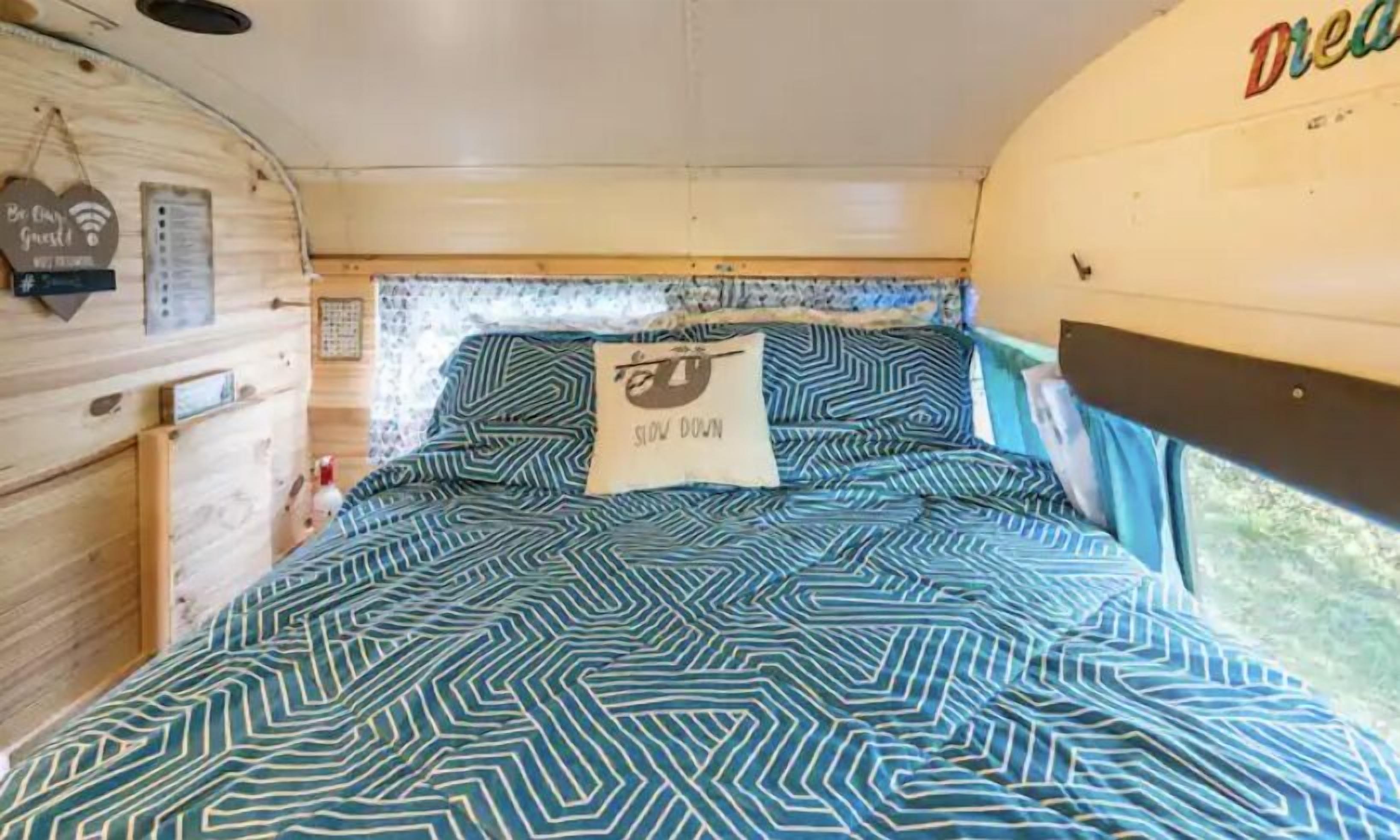 A cozy bed with a geometric patterned bedspread and a pillow with a sloth graphic and the text "SLOW DOWN".