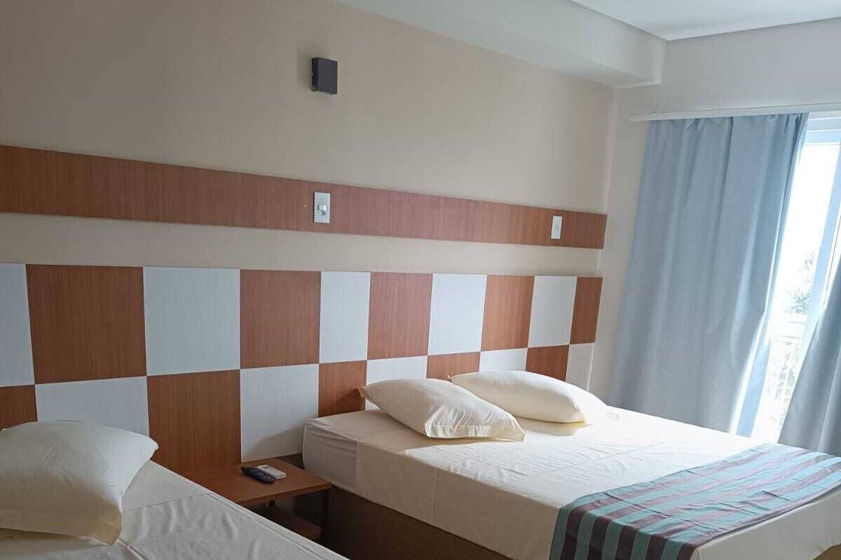 Habitación de hotel con dos camas, suelo de madera, cabecero a cuadros y una ventana con cortinas.
