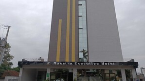 Exterior del hotel Maestro Executive, con diseño moderno, que presenta una llamativa banda vertical y una entrada amplia.