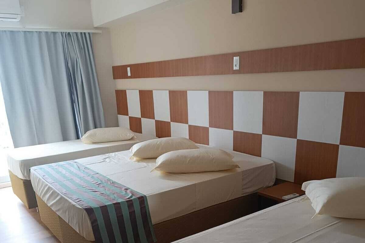 Habitación de hotel con tres camas individuales, un cabecero de madera y una ventana con cortinas.