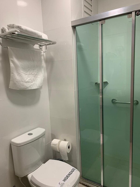Une salle de bain comprenant des toilettes, une cabine de douche en verre et un porte-serviettes avec une serviette blanche.