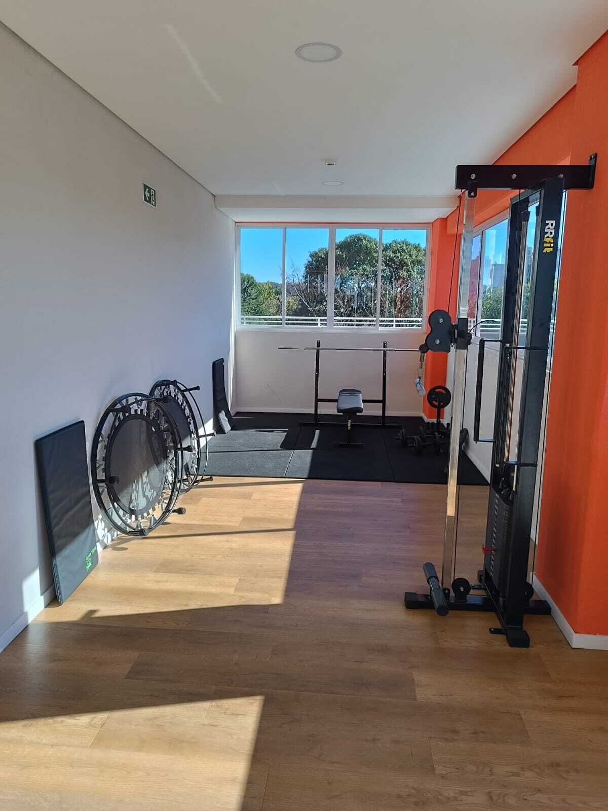 A gym with exercise equipment, a window with a view, and a door with an exit sign.
