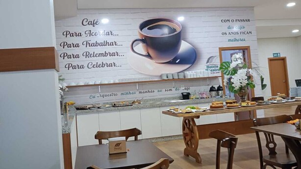 Un área de café con un gran anuncio en la pared, mesas y sillas de madera, y un mostrador con alimentos.