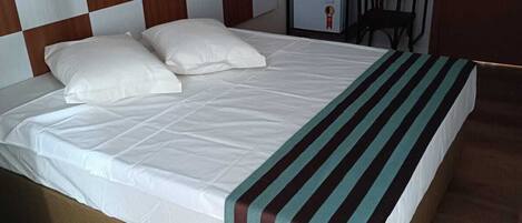 Una cama con una colcha a rayas, un cabecero de madera con estampado de cuadros y una mesita con una silla al lado.