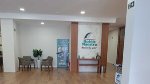 Un vestíbulo espacioso con suelo de madera, un mostrador de recepción y un cartel que dice 'Hotéis Maestro'.