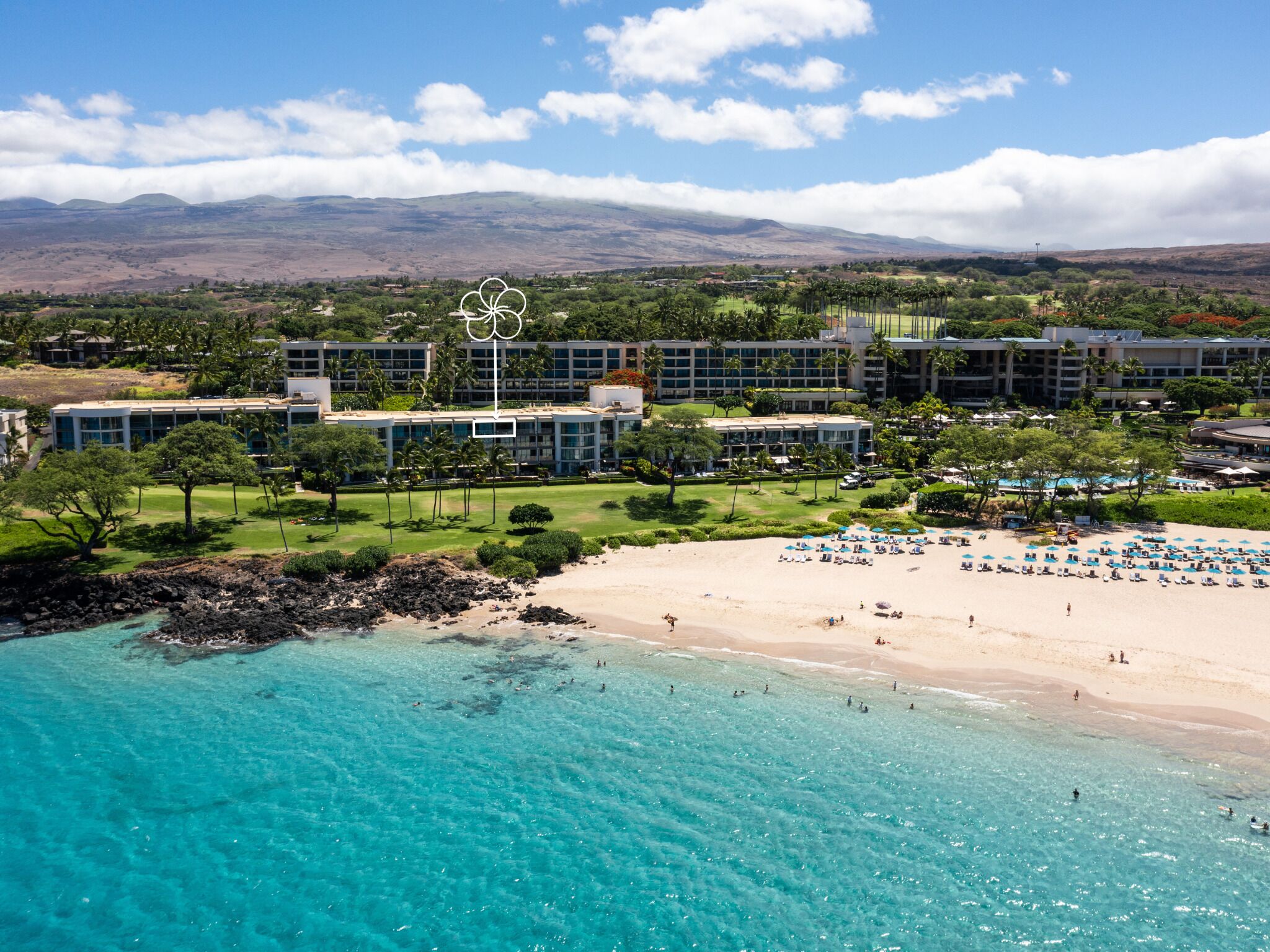 Um resort com praia, águas turquesa cristalinas e montanhas ao fundo.